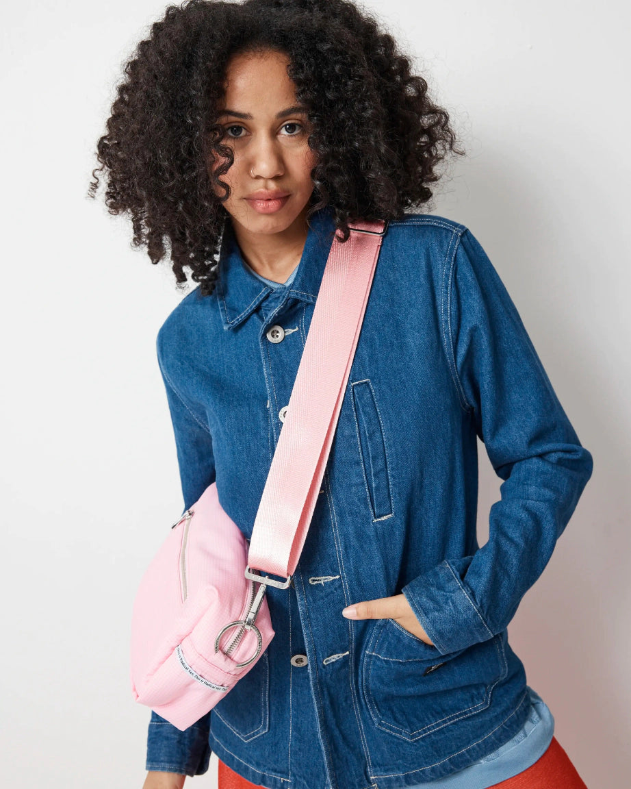Woman wearing a blue denim jacket with a pink crossbody bag against a plain background