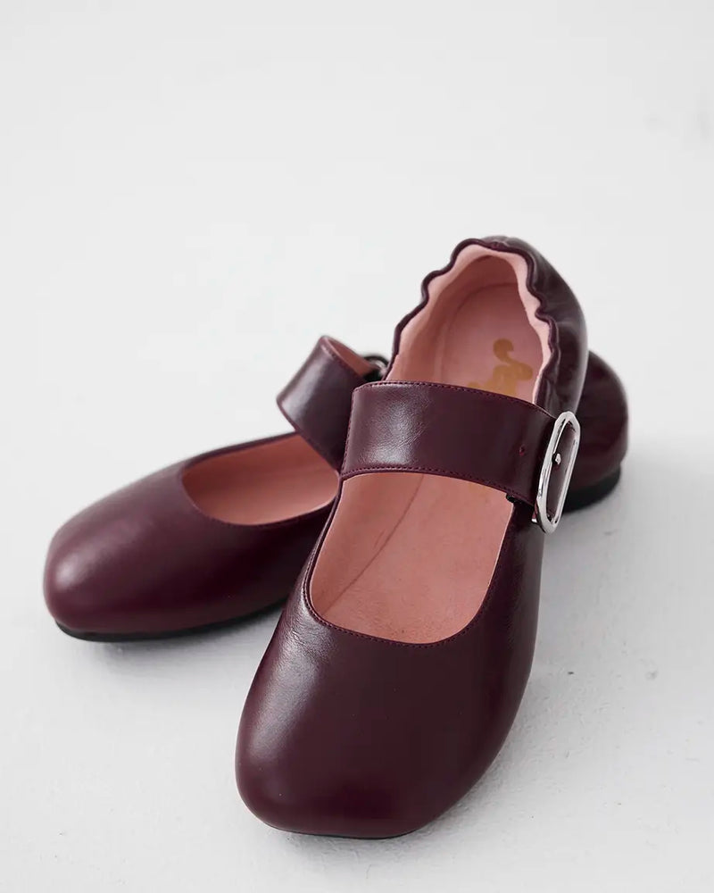A pair of burgundy leather Mary Jane shoes with ruched back, and a silver buckle.