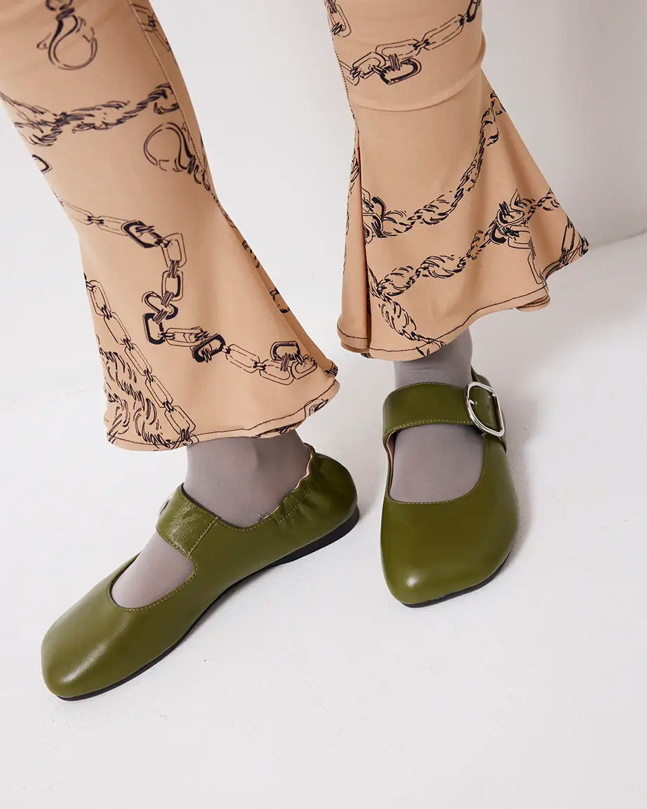 Green leather flat shoes worn with beige pants featuring a chain pattern on a white background