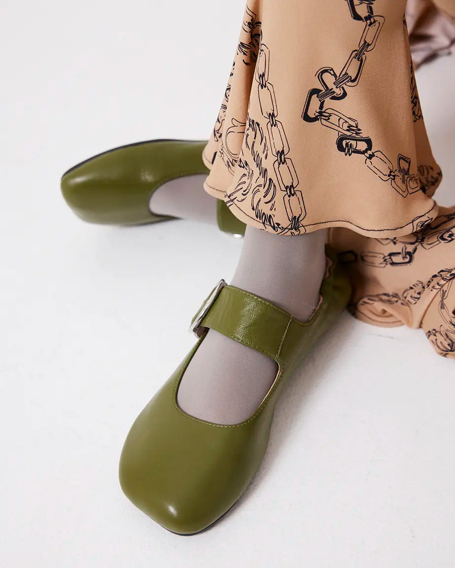 Green leather flat shoes worn with a beige skirt featuring black chain pattern on a white background