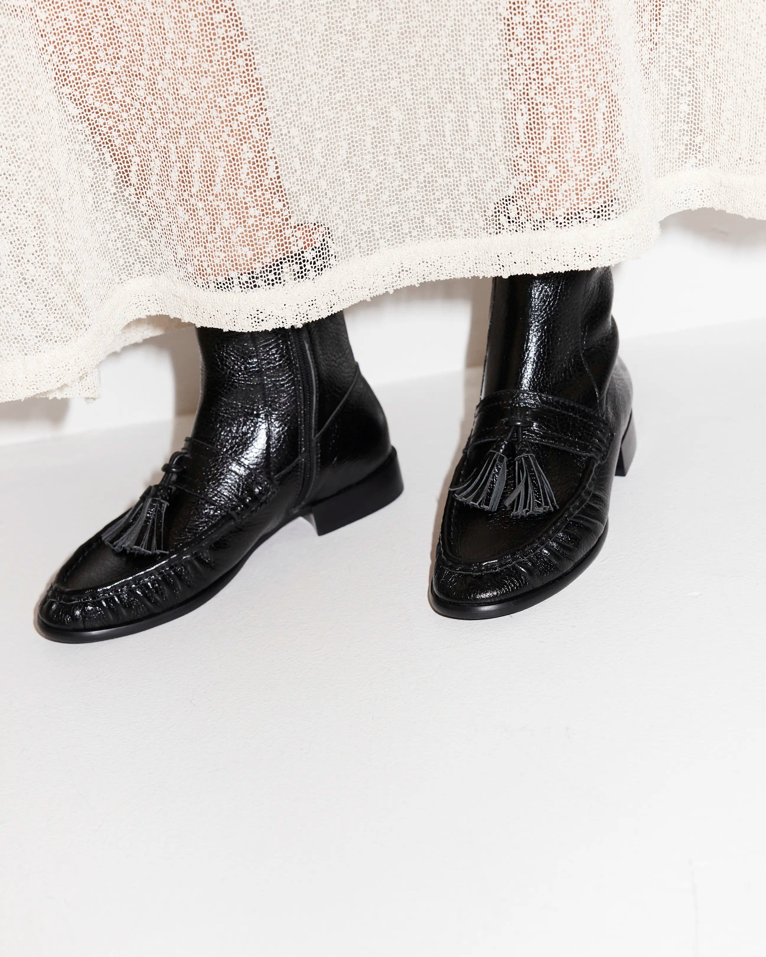 Black leather boots with tassels worn by a person on a white background