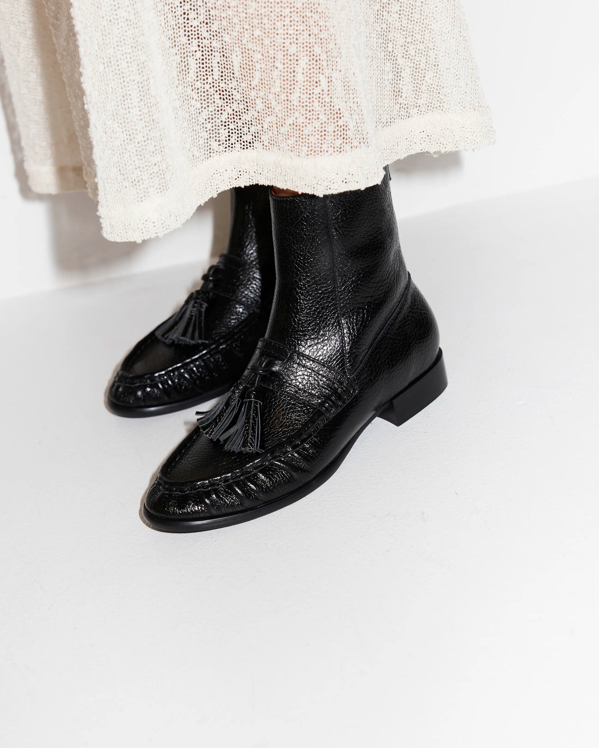 Black leather tassel boots worn with a light-coloured skirt on a white background