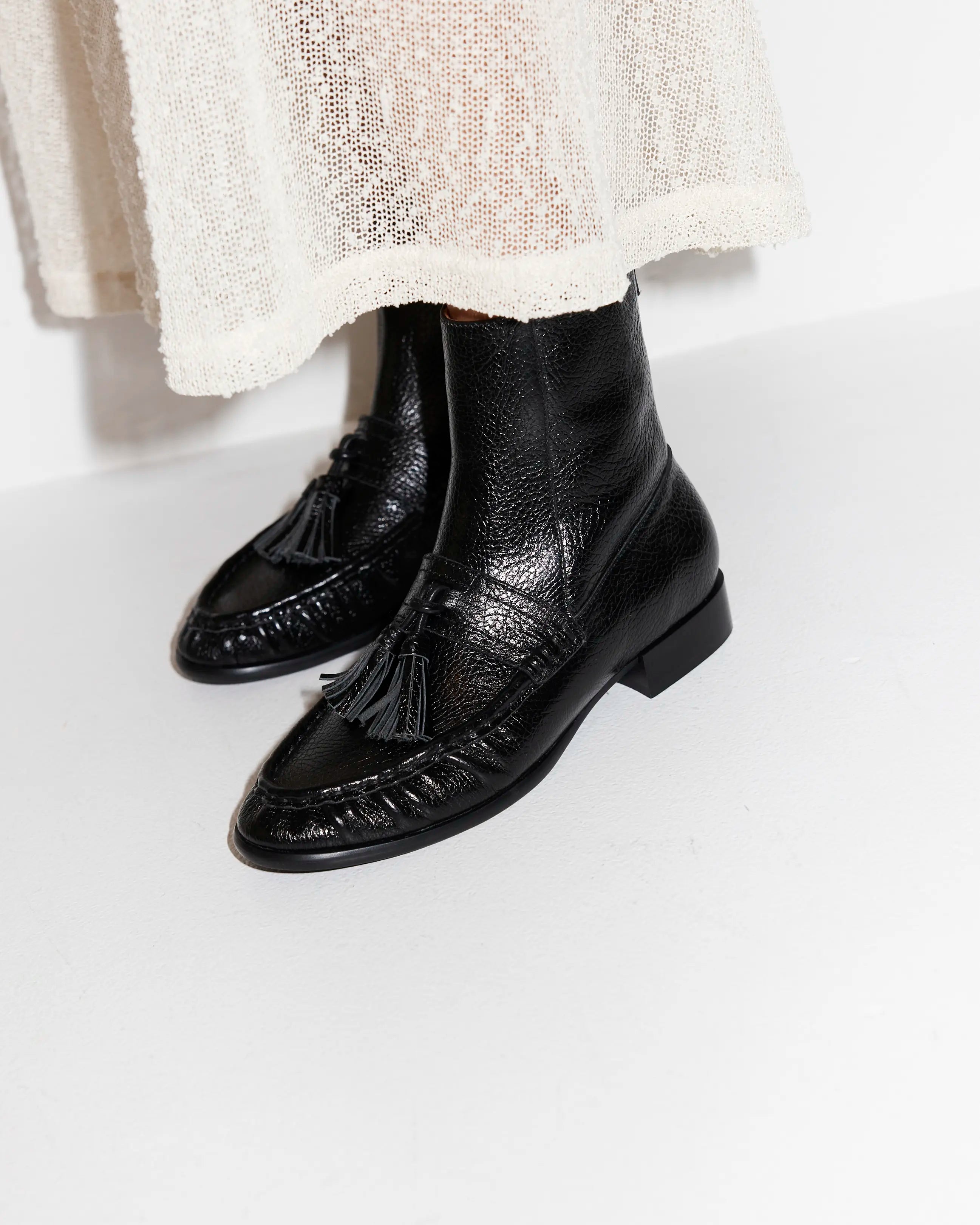 Black leather tassel boots worn with a light-coloured skirt on a white background