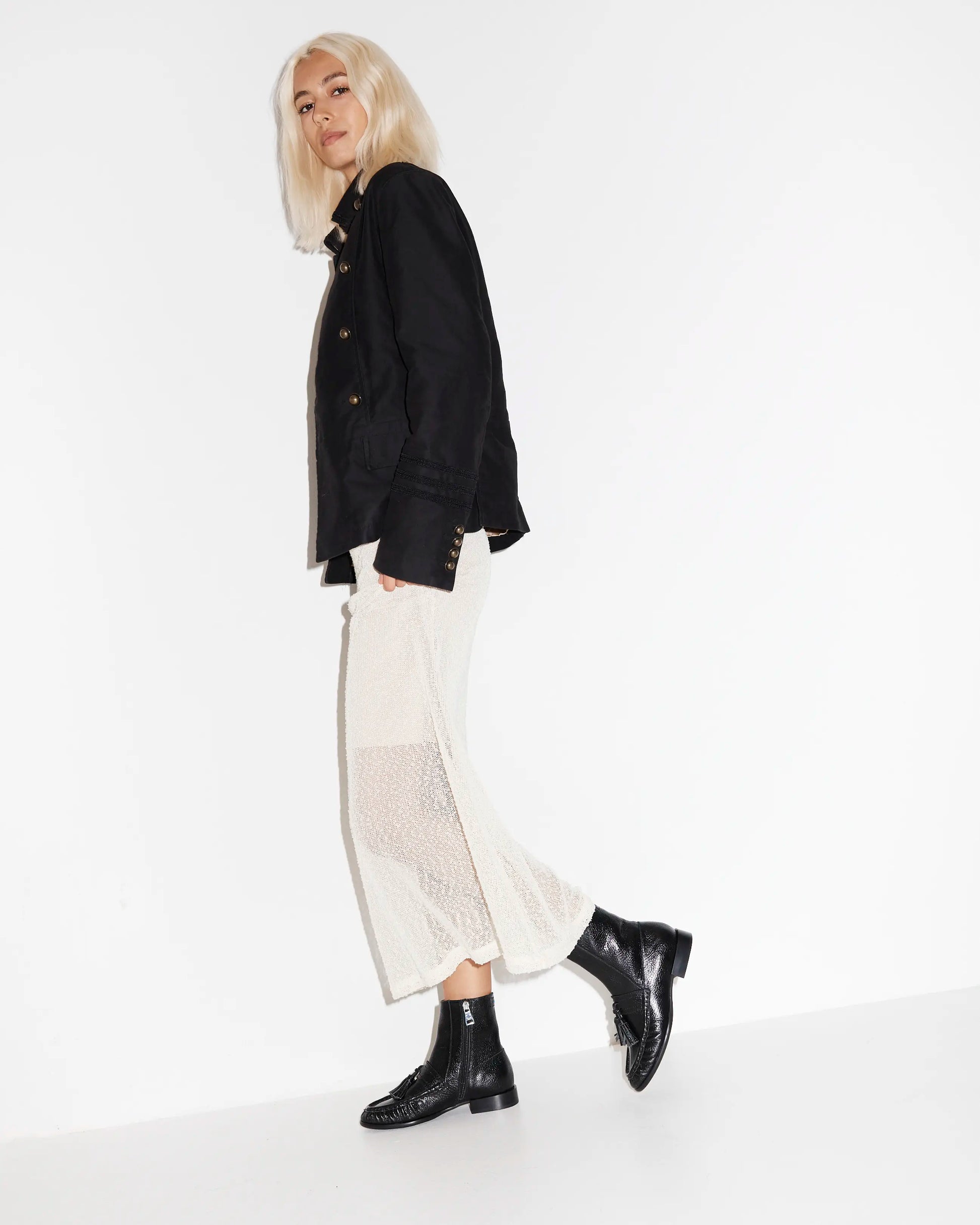 Person wearing a black jacket, white pants, and black leather boots on a white background