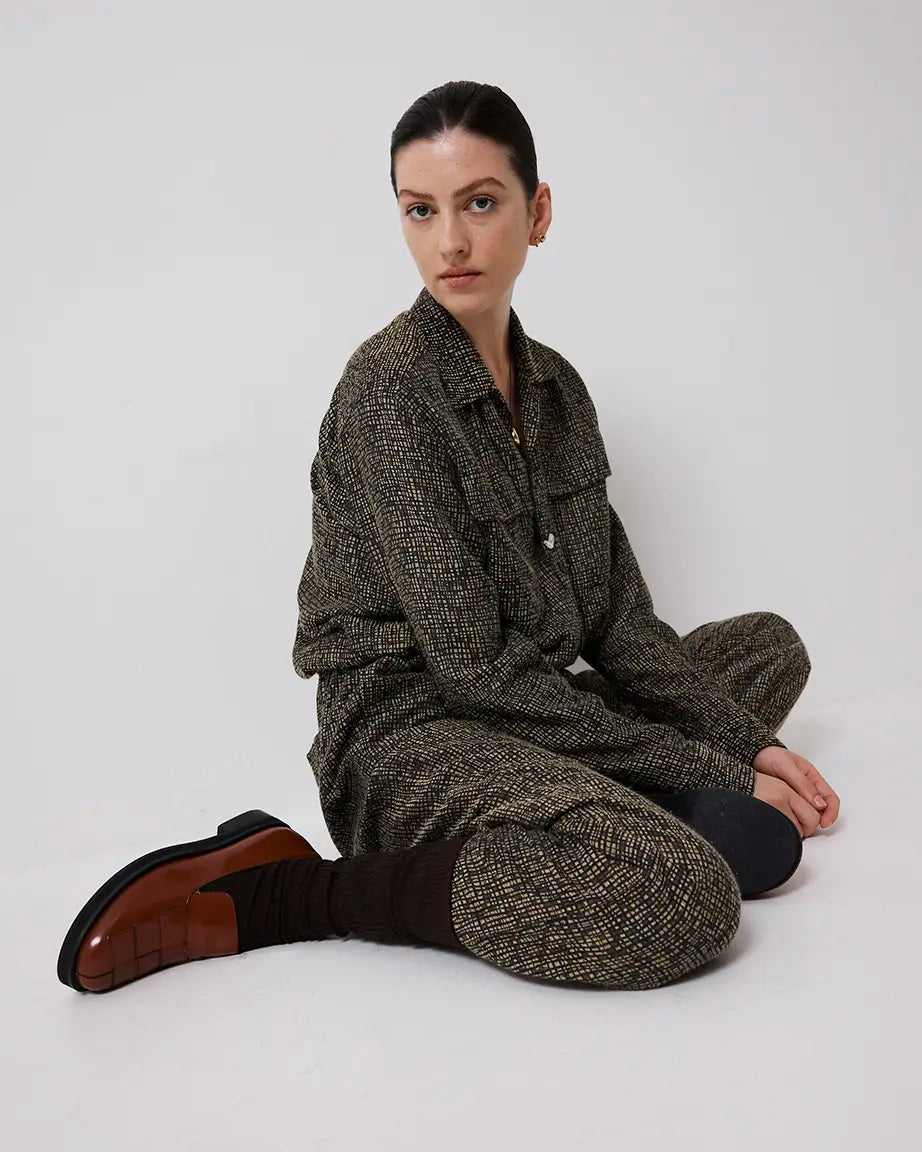 Person wearing a textured brown outfit sitting on a white background wearing brown leather loafers.