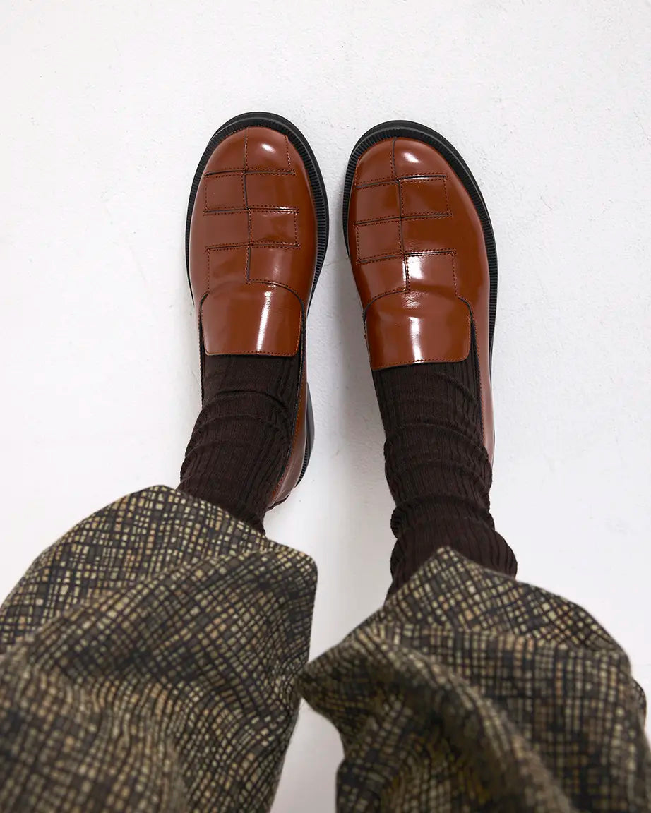 Brown leather woven shoes with black socks and plaid pants on a white background