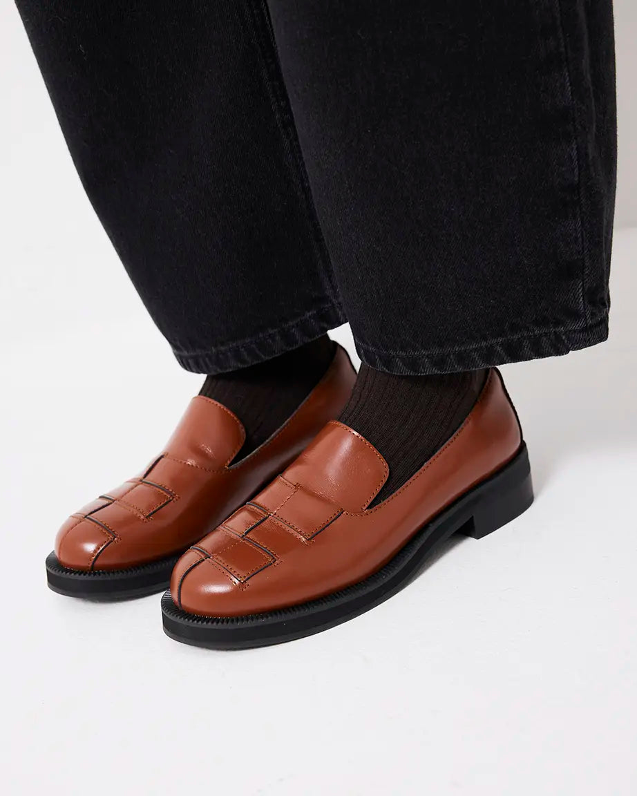 Brown leather loafers worn with black pants and socks on a white background