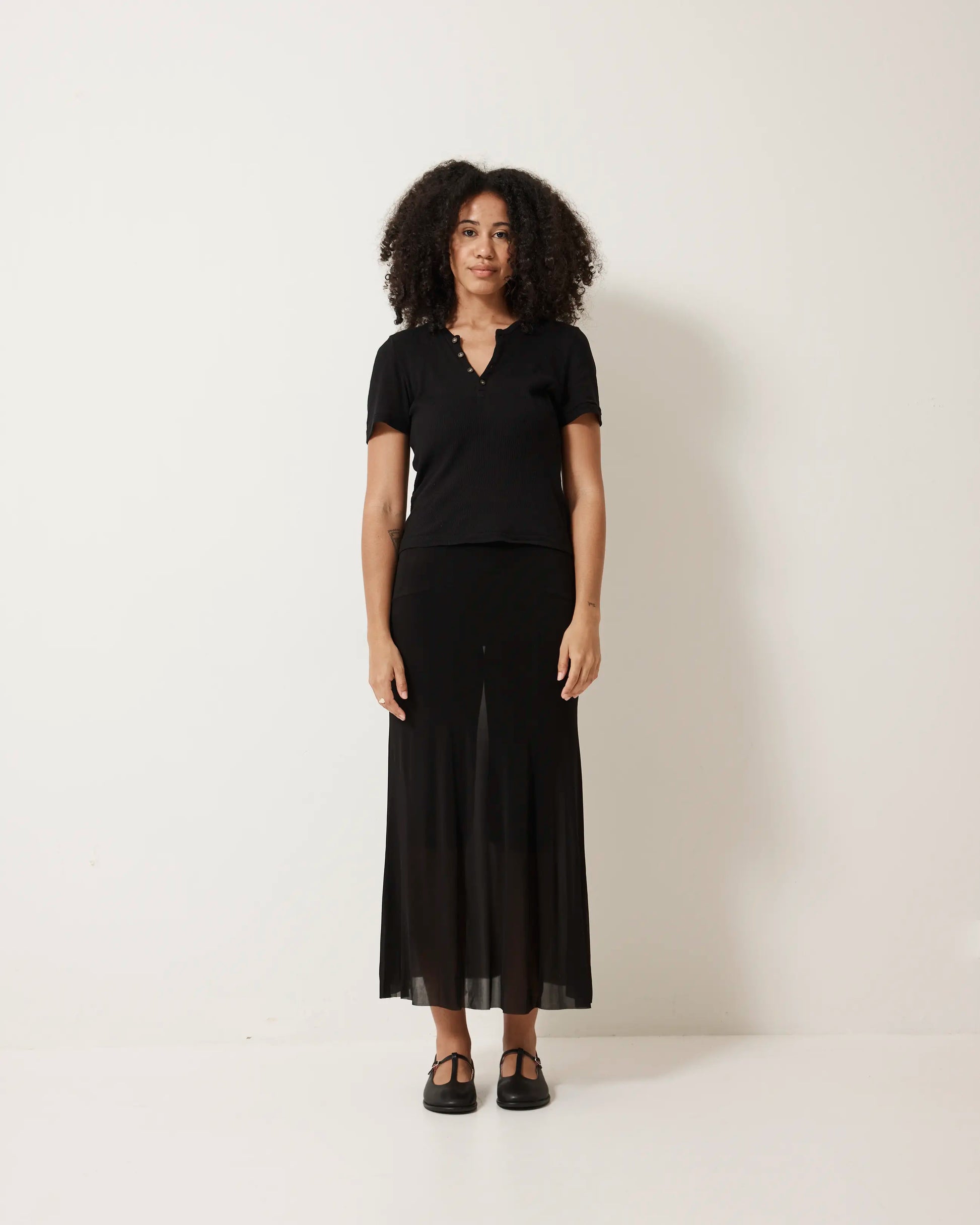 Person wearing a black outfit with black T-Bar shoes against a white background