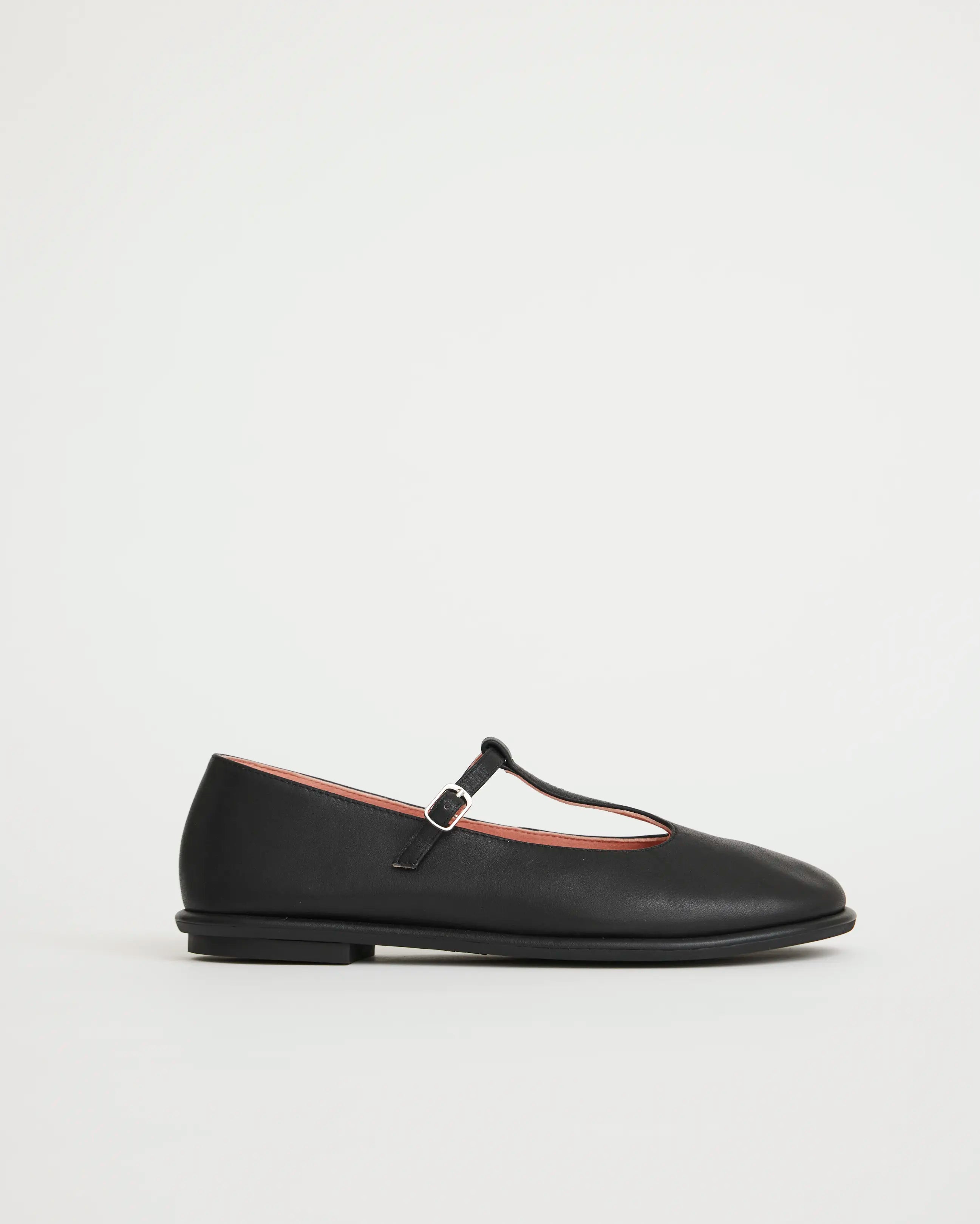 Black flat shoe with a T-Bar strap on a white background