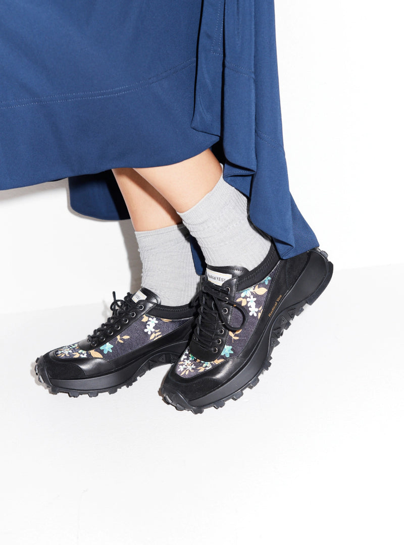 Person wearing floral printed chunky navy sneakers with grey socks and a blue skirt