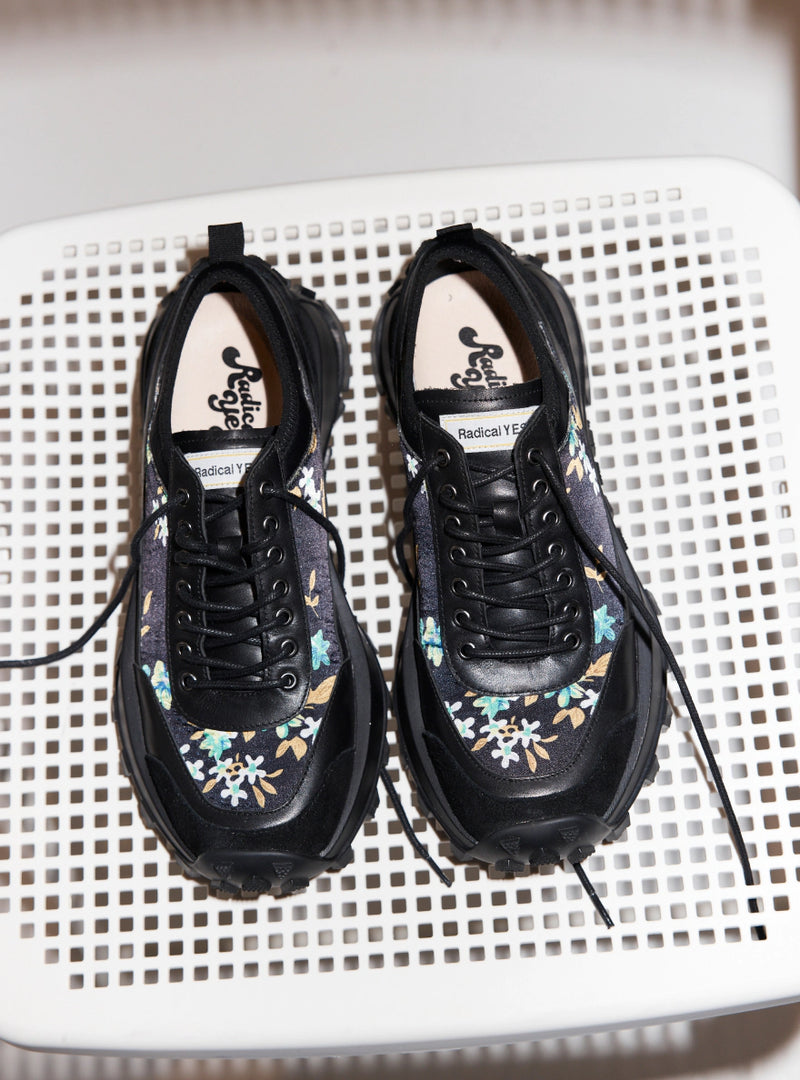 A pair of navy floral printed chunky sneakers with black laces on a white stool