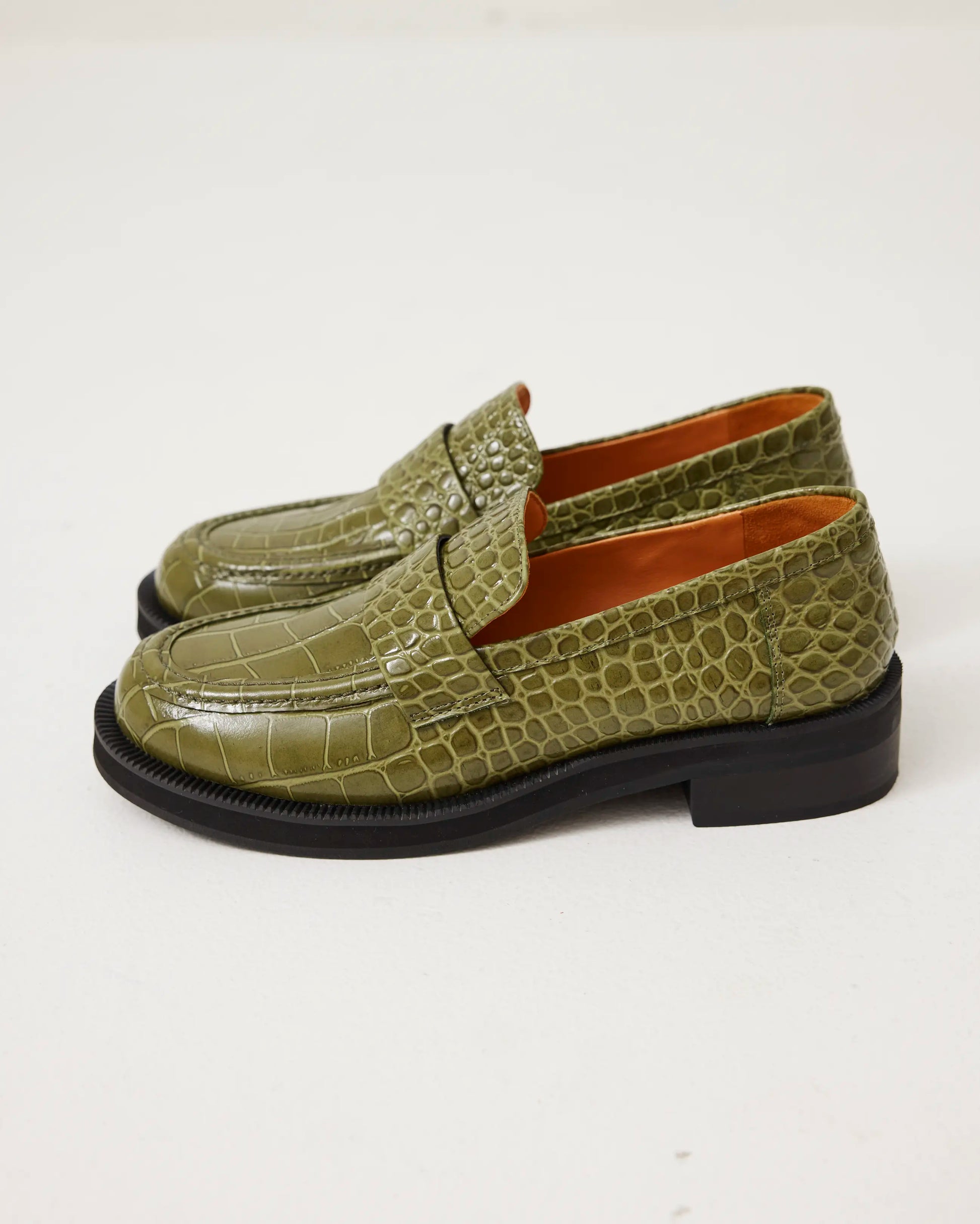 Green leather loafers with a crocodile texture on a white background