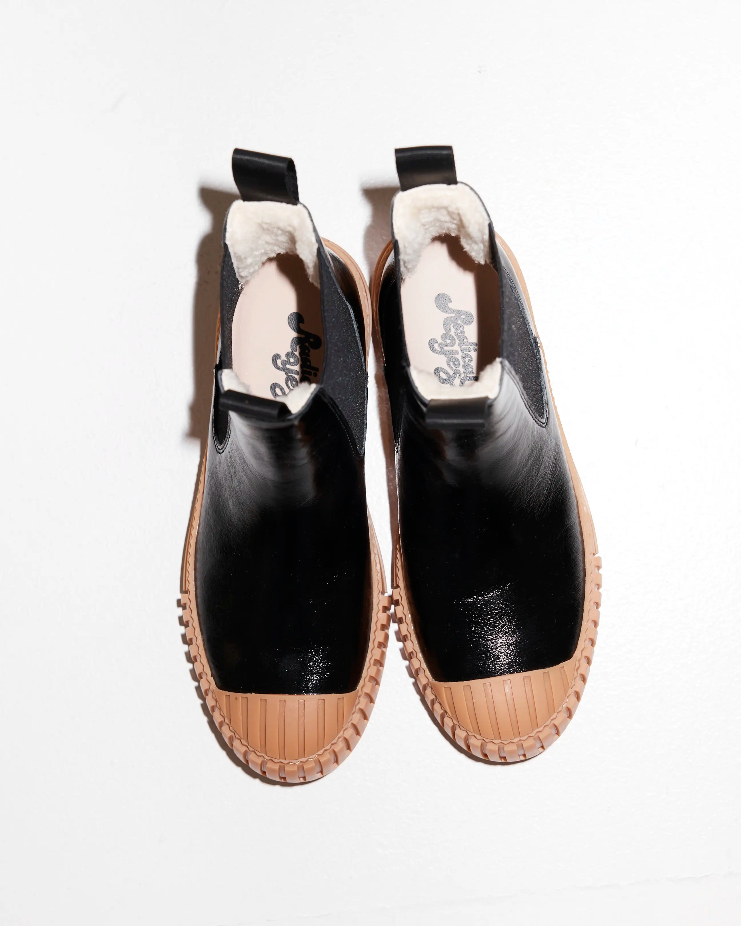 Black leather wool-lined Chelsea boots with brown soles on a white background