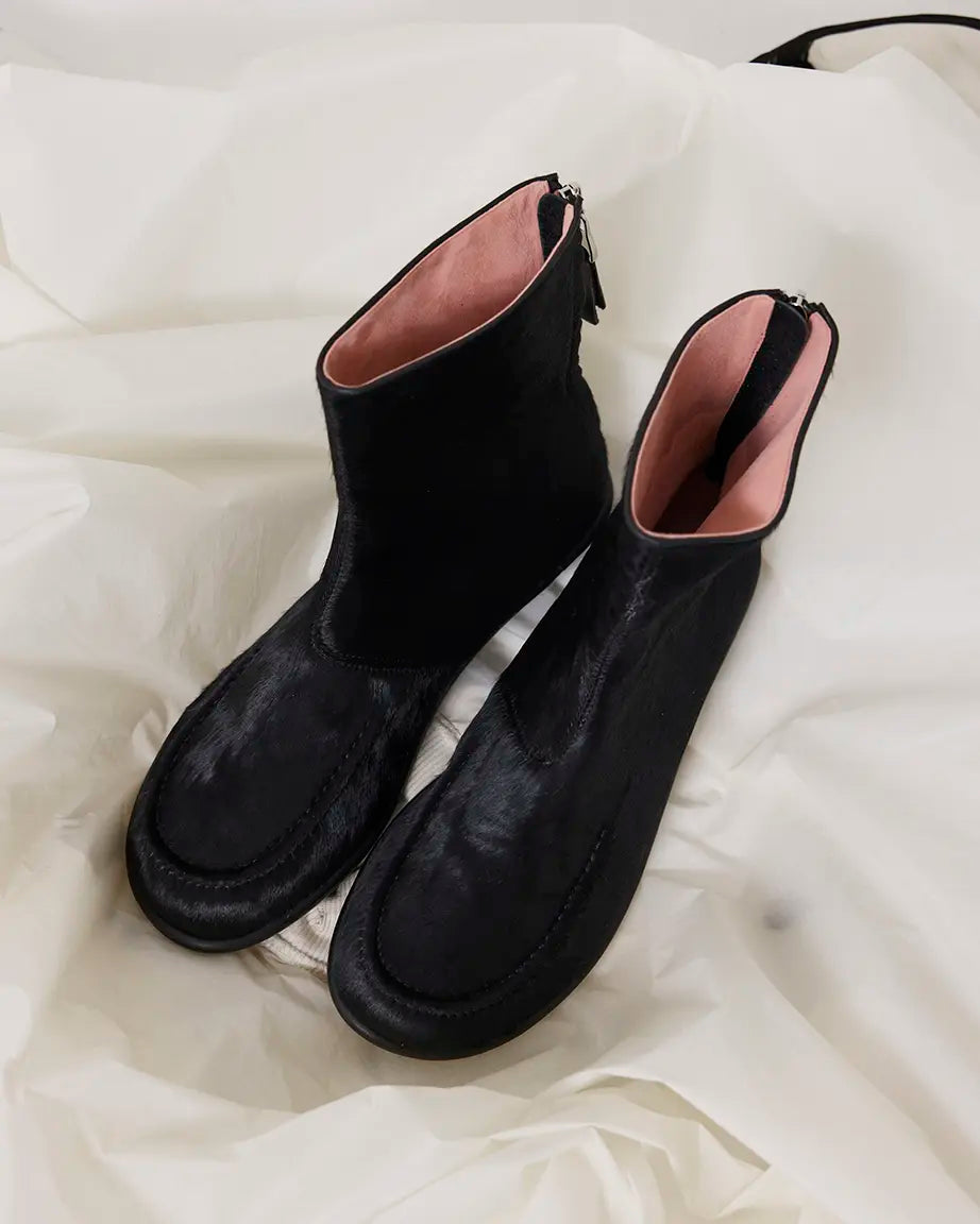 Pair of black pony hair ankle boots on a white satin background