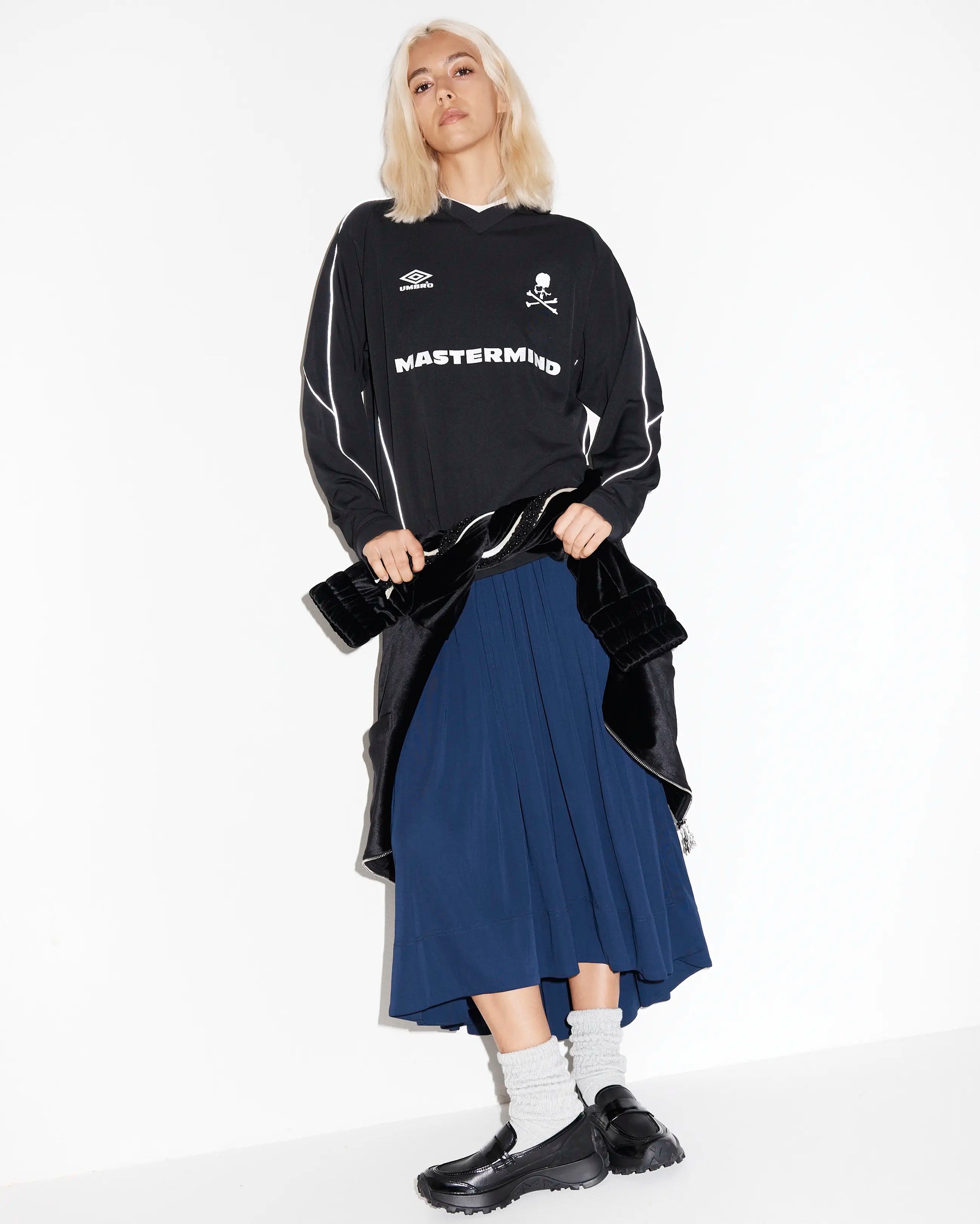 Person wearing a black jacket with chunky black leather sporty loafers on a white background