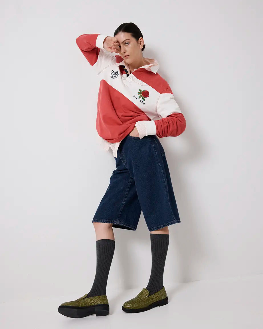 Person wearing a red and white striped sweater with a logo, dark blue pants, and green crocodile-textured leather loafers on a white background