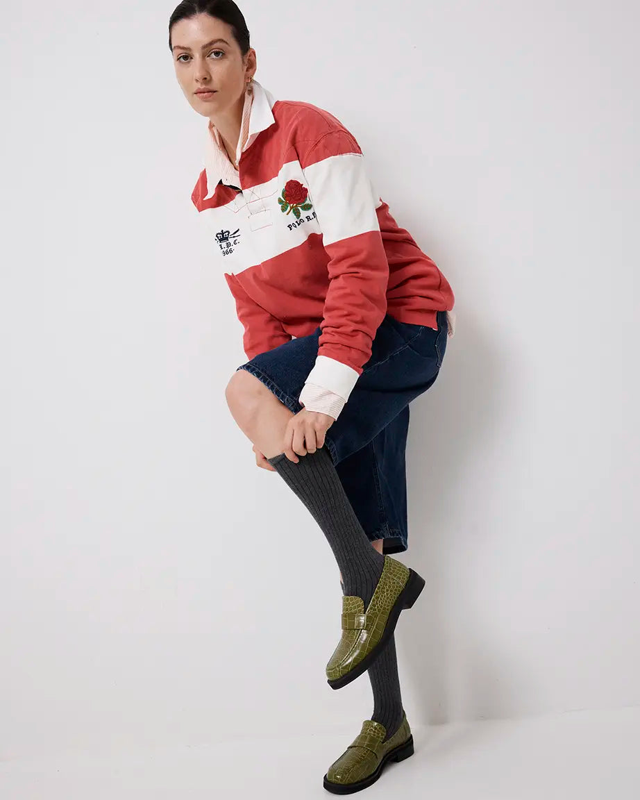 Person wearing a red and white striped sweater with a rose emblem, dark jeans, and green crocodile-textured leather loafers on a white background.