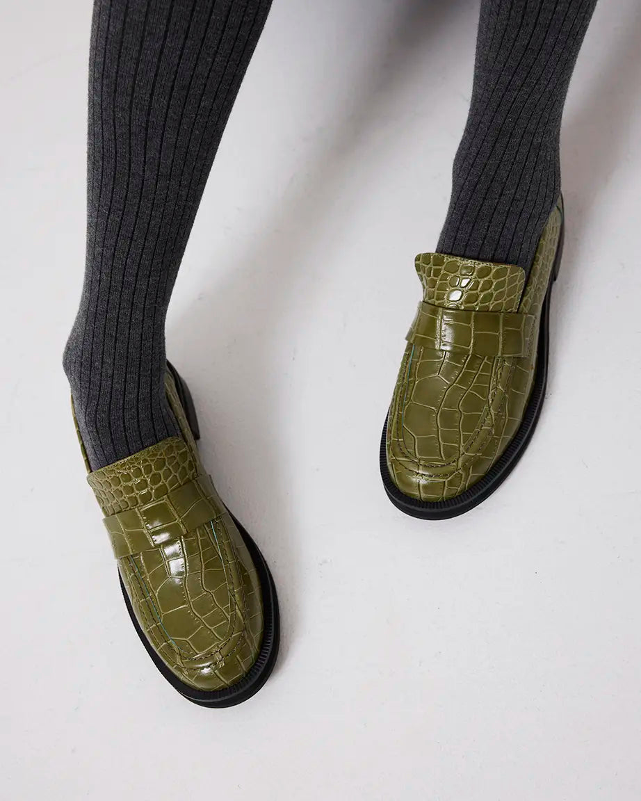 Green crocodile-textured leather loafers worn with gray socks on a white background