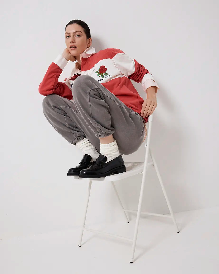 Person wearing a red and white sweater with gray pants and black leather loafers sitting on a white chair against a white background