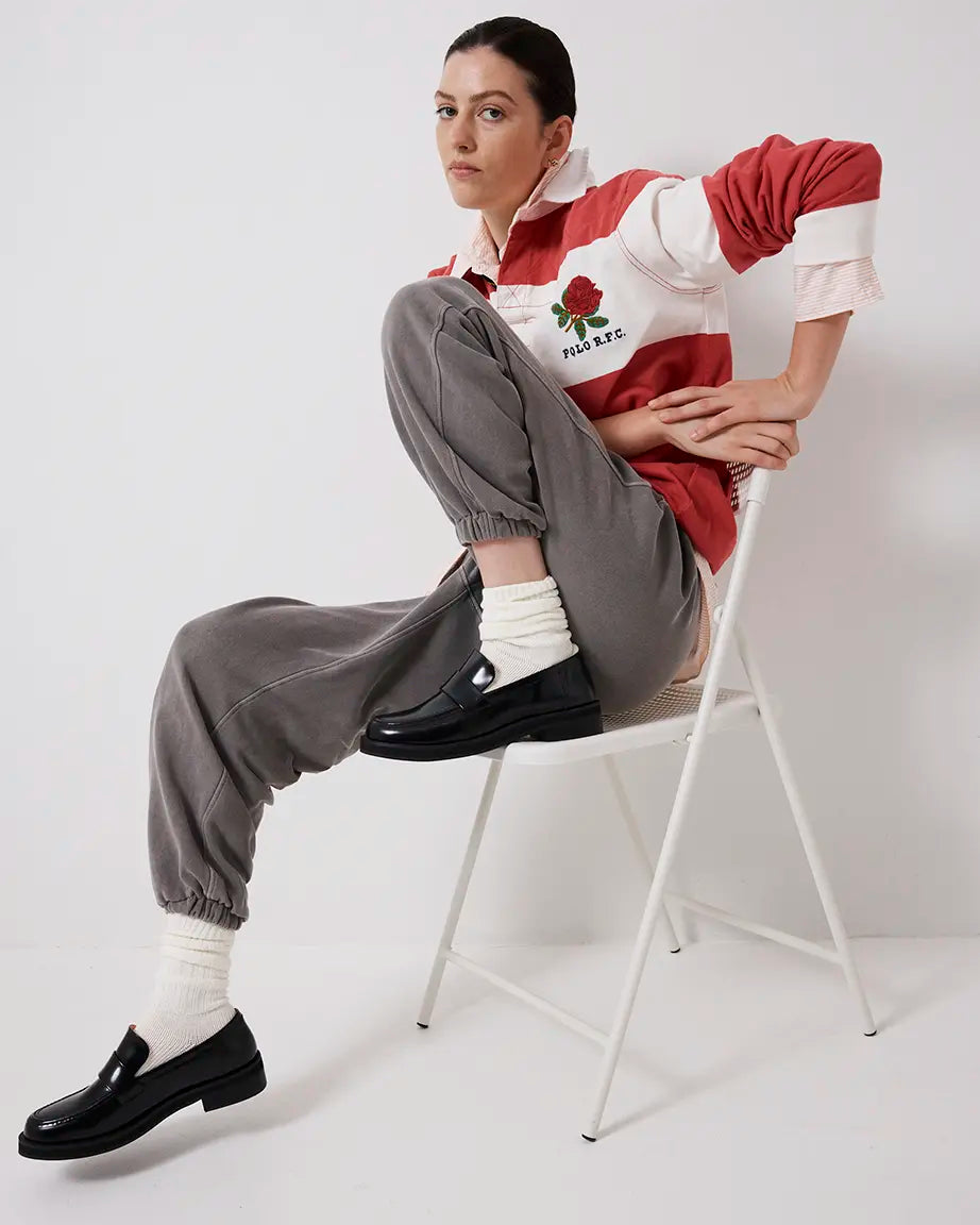Person wearing a red and white striped shirt with gray pants and black leather loafers sitting on a chair against a white background