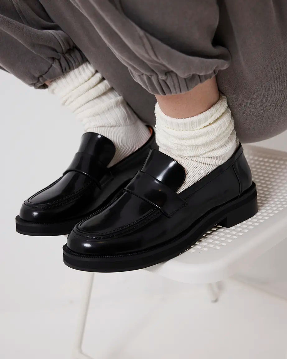 Person wearing black leather loafers and white socks on a light background