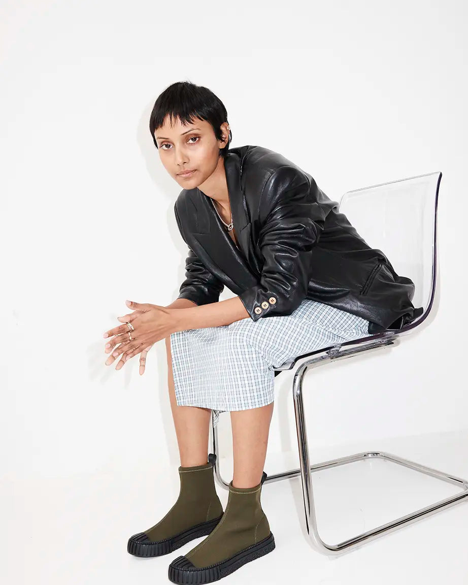 A model sits on a clear acrylic chair wearing olive green ankle boots