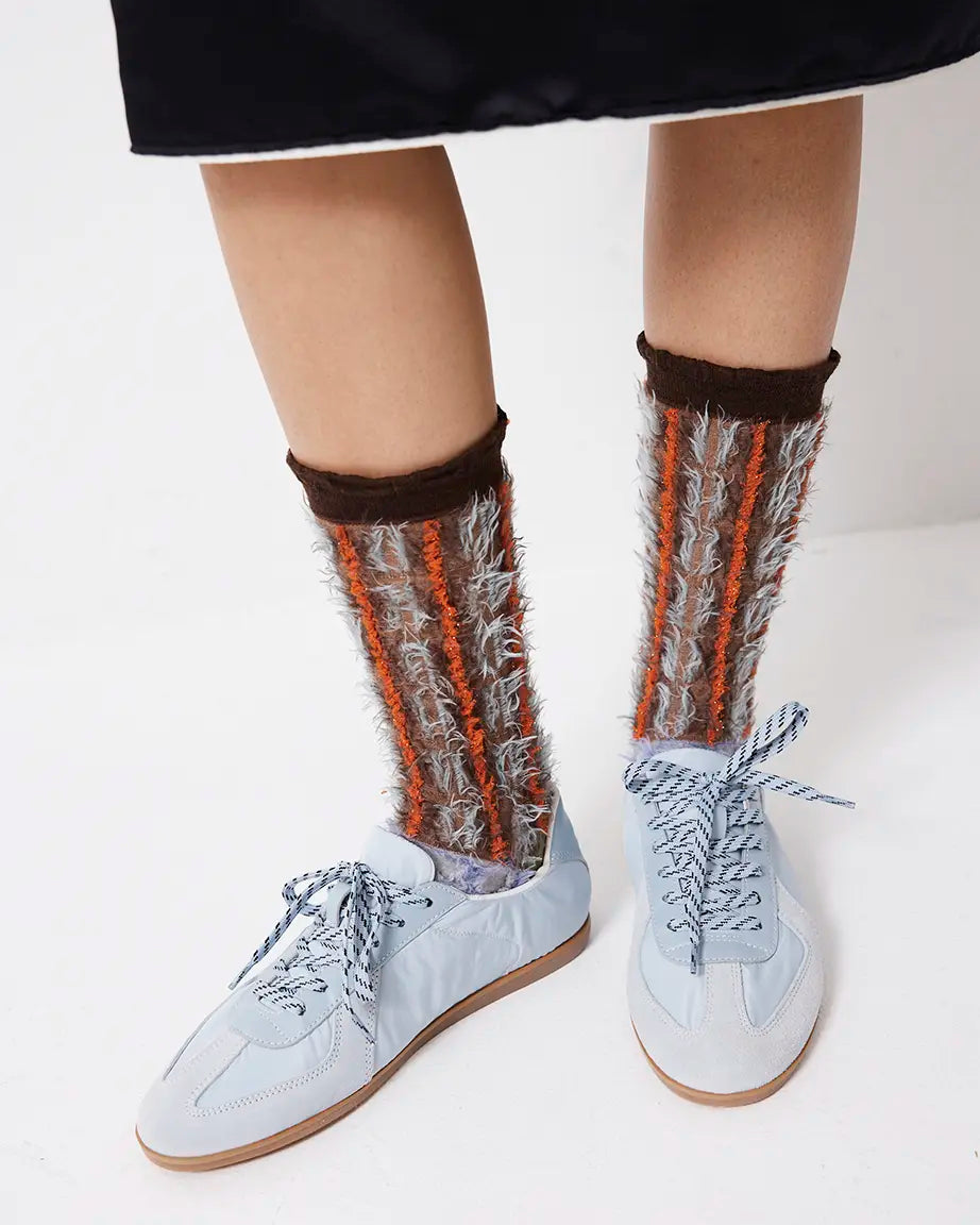 Person wearing patterned socks with brown and orange stripes and light blue sneakers against a white background