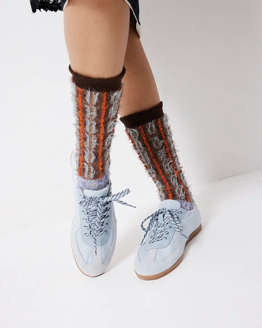 Person wearing light blue sneakers with patterned socks on a plain background