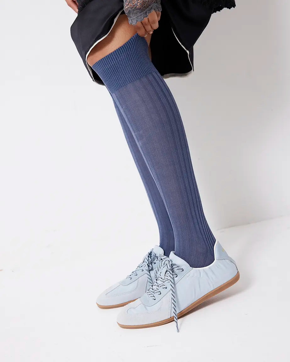Person wearing blue knee-high socks and light blue sneakers on a plain background