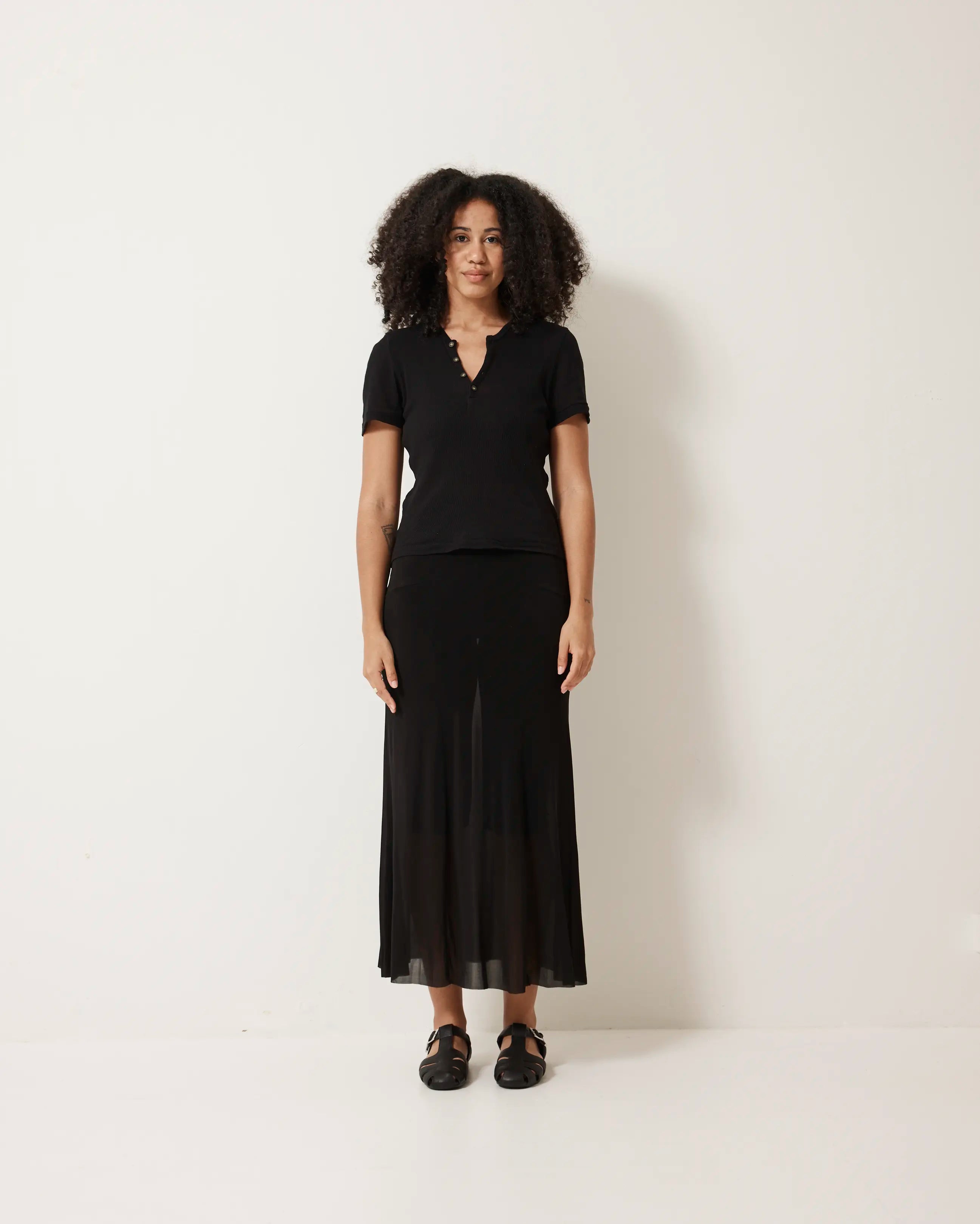 Woman wearing a black top and black skirt with black fisherman sandals on a white background