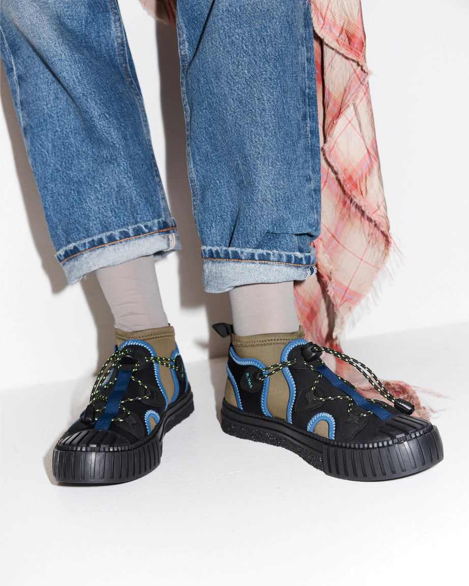 Person wearing an olive and black neoprene sneaker with blue denim.
