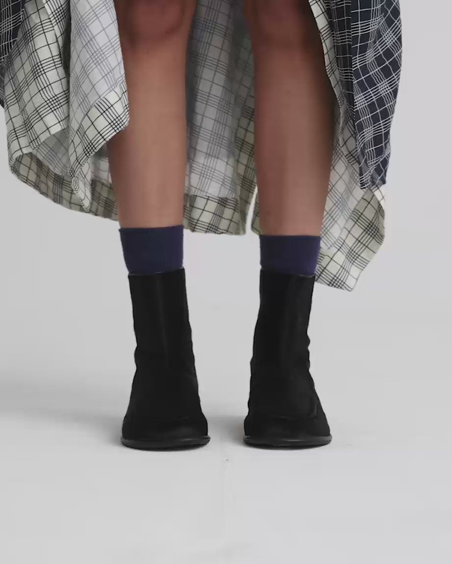 Load video: Person wearing black pony hair ankle boots with blue socks and patterned skirt against a white background.
