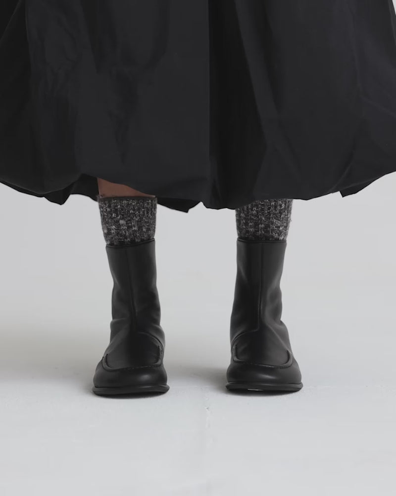 Person wearing black leather ankle boots with patterned socks and black skirt against a white background.