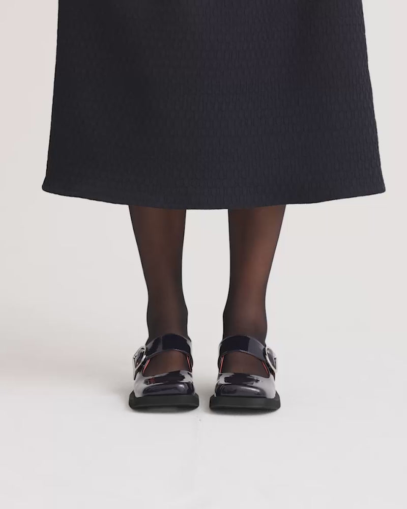 Glossy navy leather square toe shoes with silver buckles worn with black stockings