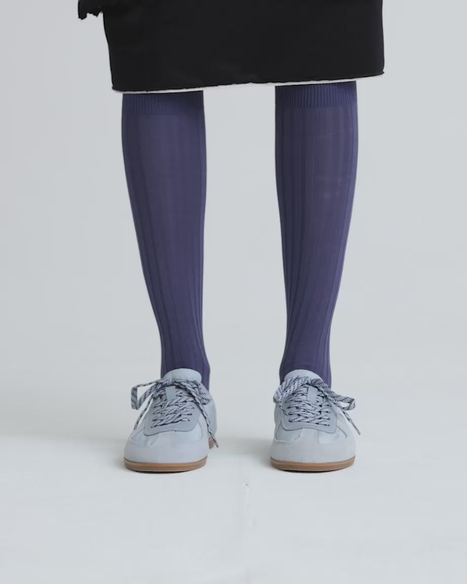 Load video: Person wearing blue knee high socks and light blue sneakers against a white background.