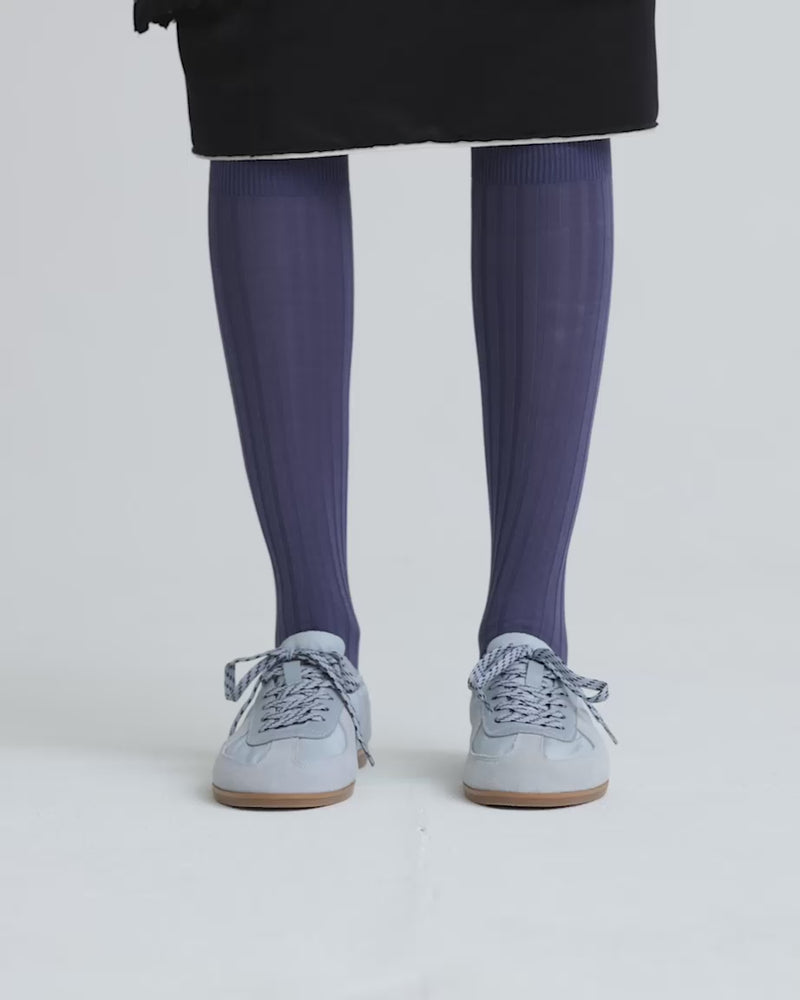Person wearing blue knee high socks and light blue sneakers against a white background.