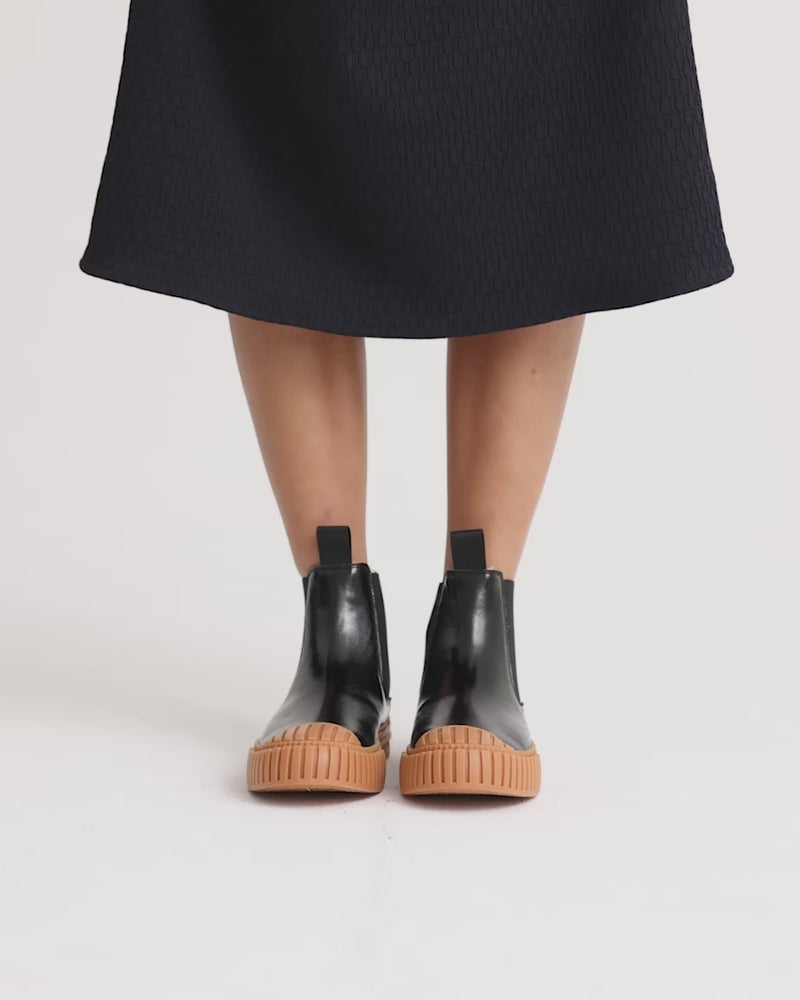 Person wearing black leather wool-lined Chelsea boots with brown soles