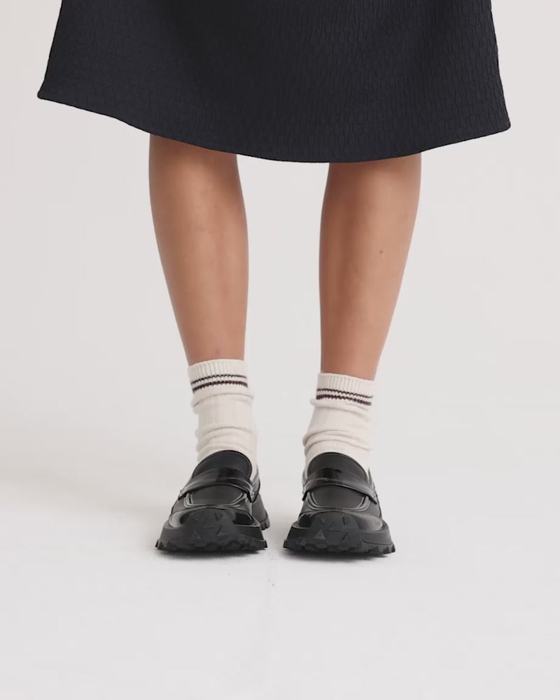 Person wearing chunky black leather loafers with white socks