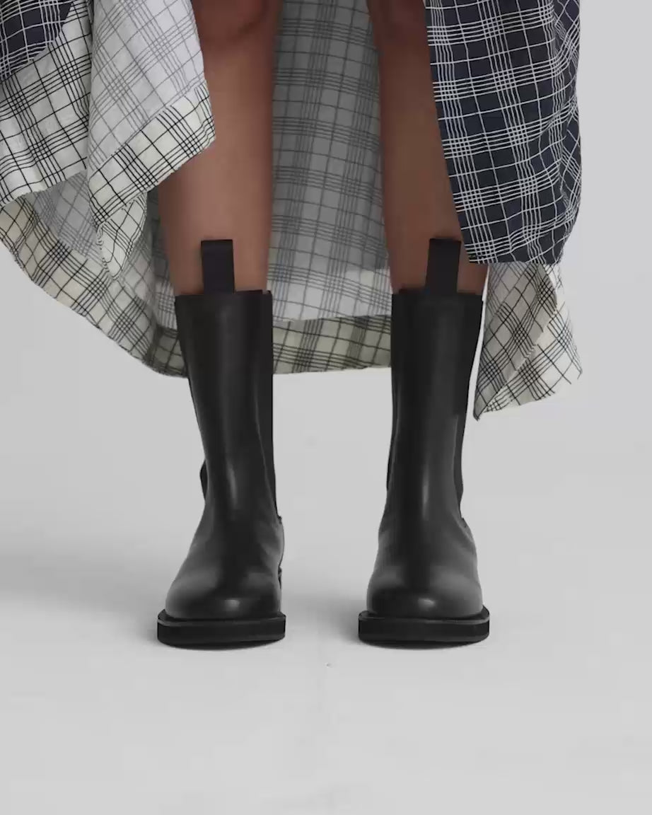 Load video: Person wearing black leather riding boots with a patterned skirt.