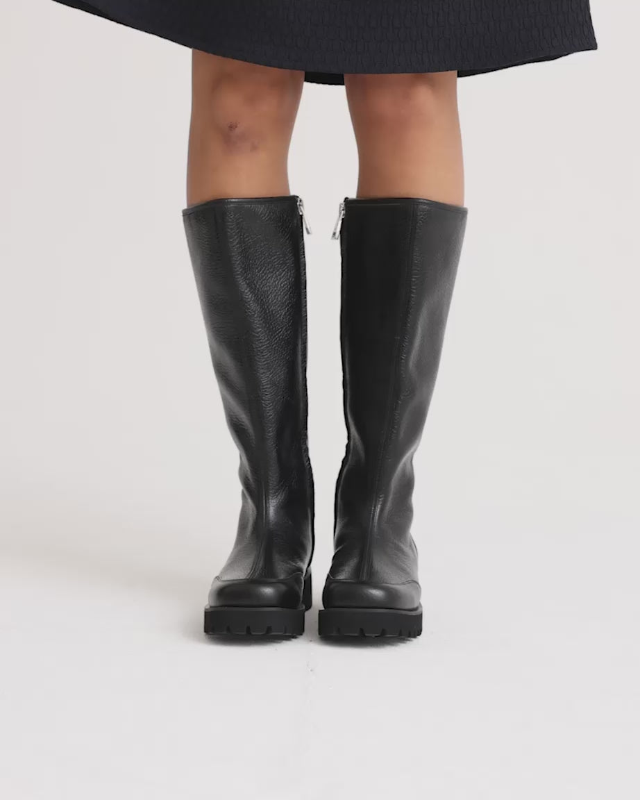 Load video: Person wearing black leather knee high boots with a side zip