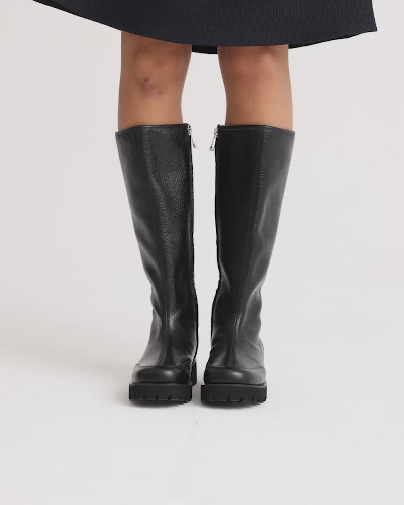 Person wearing black leather knee high boots with a side zip