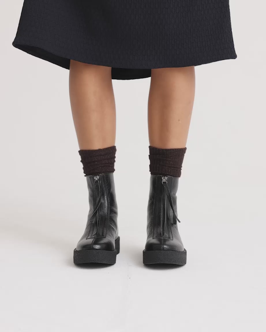 Load video: Black leather zip up ankle boots worn with brown socks.